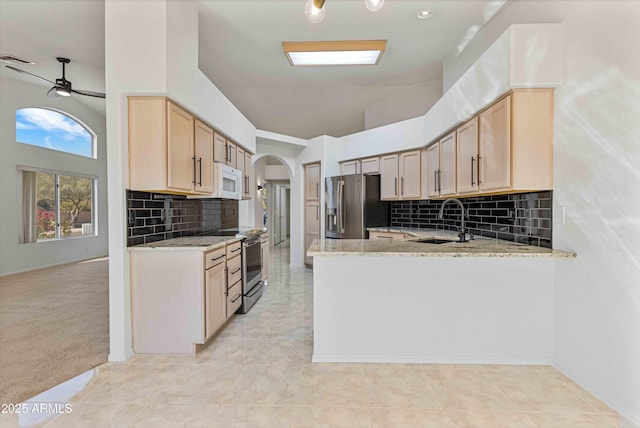 kitchen featuring arched walkways, stainless steel appliances, light stone counters, and a sink