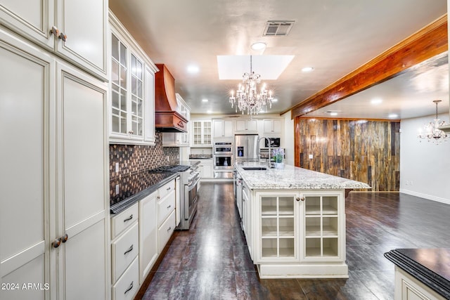 kitchen featuring premium range hood, dark wood-type flooring, hanging light fixtures, an island with sink, and appliances with stainless steel finishes