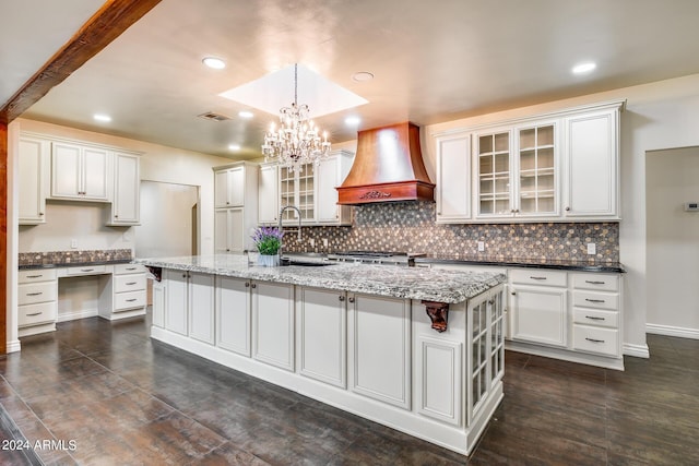 kitchen featuring dark stone counters, decorative light fixtures, a kitchen island with sink, white cabinets, and custom exhaust hood