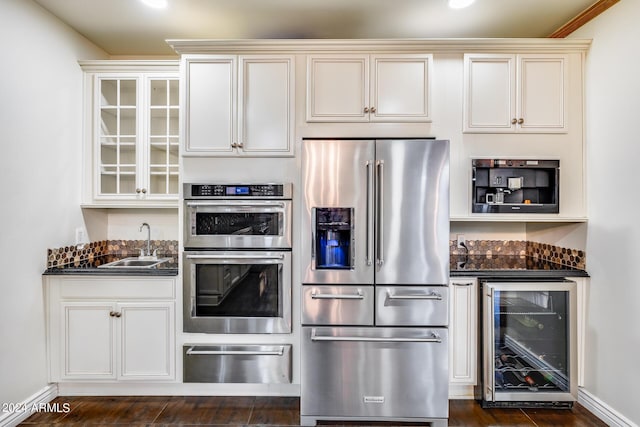 kitchen with ornamental molding, dark stone counters, stainless steel appliances, sink, and wine cooler