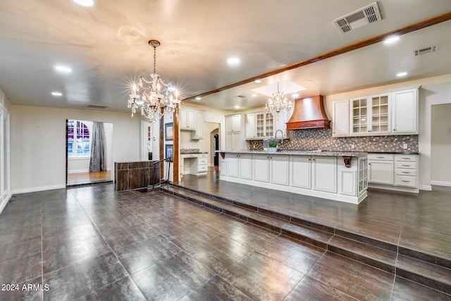 kitchen with pendant lighting, a kitchen island with sink, white cabinets, decorative backsplash, and custom range hood