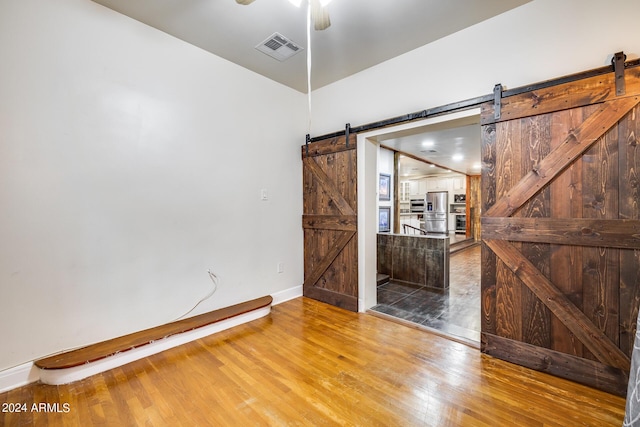 unfurnished room featuring hardwood / wood-style floors, a barn door, and ceiling fan