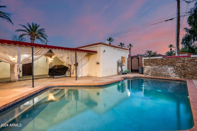 pool at dusk featuring a patio area, a grill, and water heater