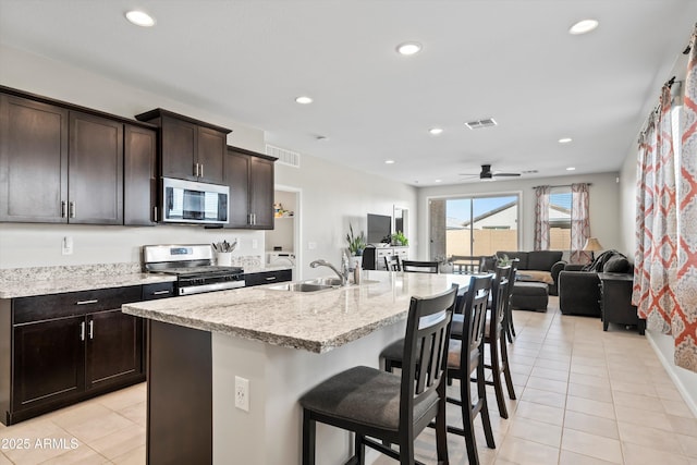 kitchen featuring sink, appliances with stainless steel finishes, a kitchen island with sink, a kitchen breakfast bar, and dark brown cabinetry