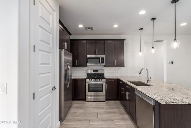 kitchen with dark brown cabinetry, stainless steel appliances, a peninsula, a sink, and visible vents