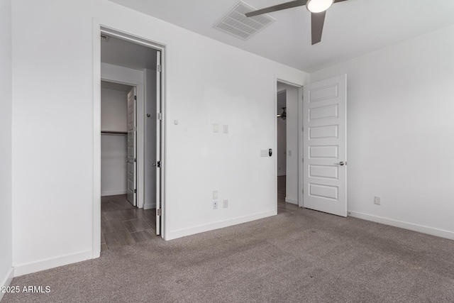 unfurnished bedroom with carpet, visible vents, a spacious closet, a ceiling fan, and baseboards