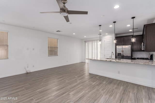 kitchen featuring stainless steel fridge, visible vents, decorative backsplash, dark brown cabinets, and a sink