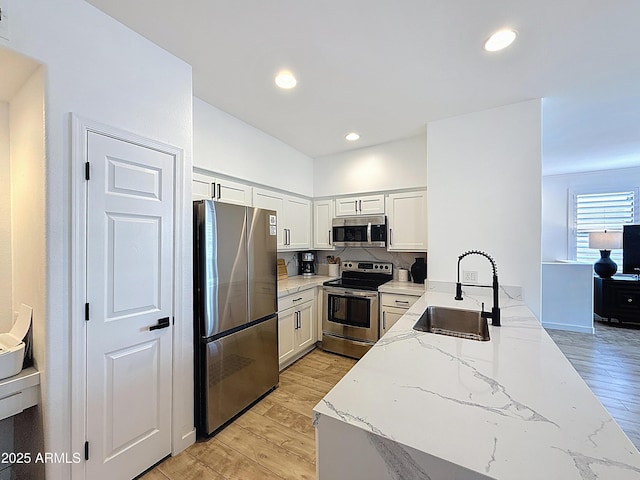 19777 N 76th St N Unit 2243, Scottsdale, AZ 85255 - kitchen with stainless steel appliances, a sink, light stone counters, light wood-style flooring, and white cabinetry
