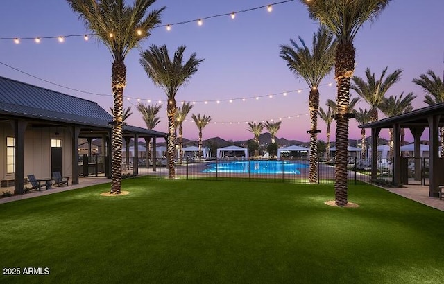 pool at dusk with a patio area, a yard, fence, and a community pool