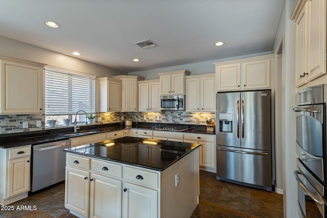 kitchen with stainless steel appliances, sink, cream cabinetry, tasteful backsplash, and a kitchen island