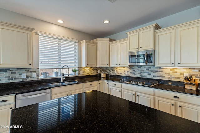 kitchen with appliances with stainless steel finishes, dark stone counters, backsplash, and sink