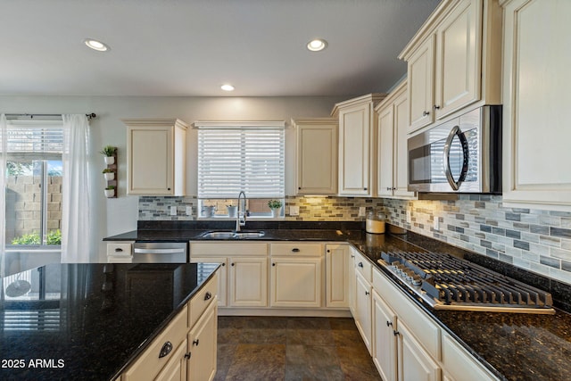 kitchen featuring appliances with stainless steel finishes, cream cabinetry, dark stone countertops, and sink