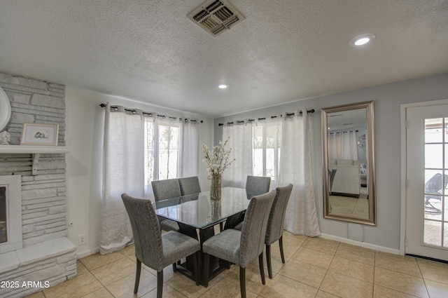 dining space with a stone fireplace, a wealth of natural light, a textured ceiling, and light tile patterned floors