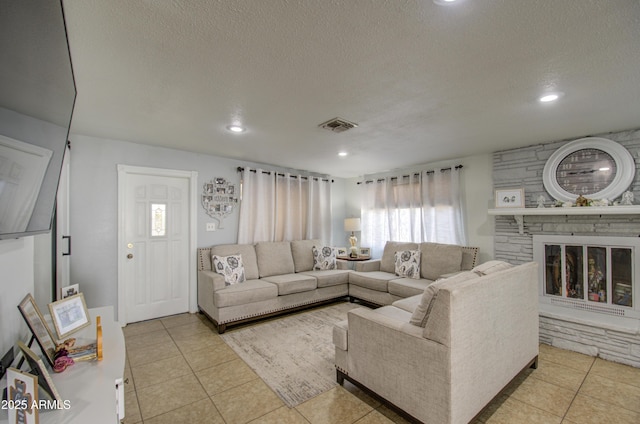 living room with light tile patterned flooring, a stone fireplace, and a textured ceiling