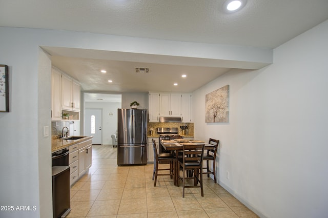 kitchen with sink, light tile patterned floors, stainless steel fridge, white cabinetry, and tasteful backsplash