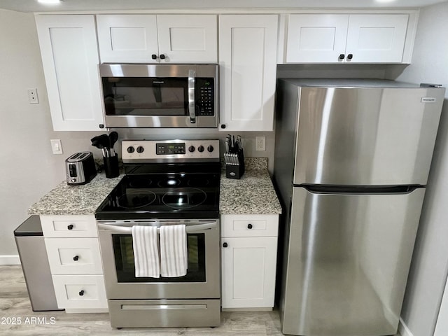 kitchen with white cabinets, light stone countertops, appliances with stainless steel finishes, and light hardwood / wood-style flooring