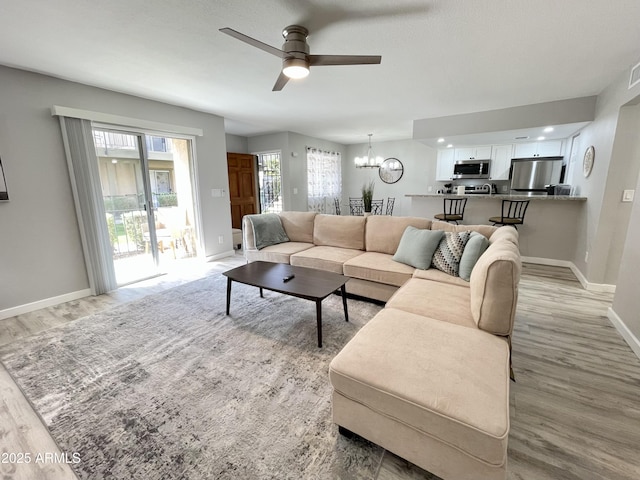 living room with ceiling fan with notable chandelier and light hardwood / wood-style floors