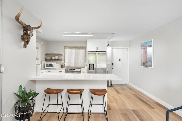 kitchen with a breakfast bar, light wood finished floors, appliances with stainless steel finishes, white cabinetry, and a peninsula