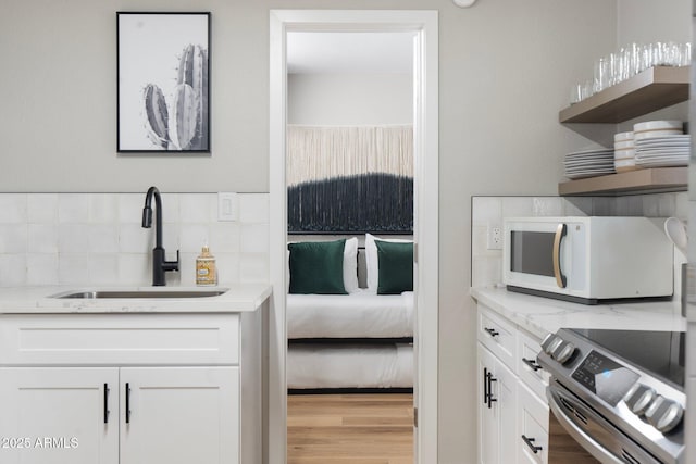 kitchen featuring white cabinets, white microwave, stainless steel electric range oven, open shelves, and a sink