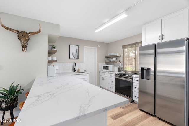 kitchen featuring light stone counters, appliances with stainless steel finishes, white cabinetry, open shelves, and a sink