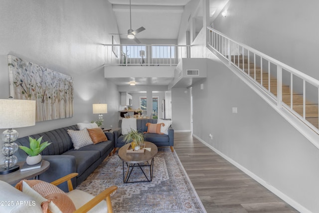 living room featuring a ceiling fan, wood finished floors, stairway, baseboards, and a towering ceiling