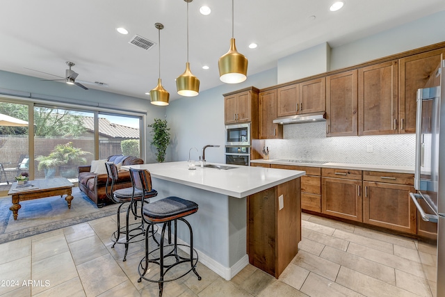 kitchen with ceiling fan, sink, stainless steel appliances, an island with sink, and decorative light fixtures