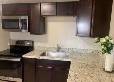 kitchen featuring sink, dark brown cabinetry, light stone countertops, and appliances with stainless steel finishes