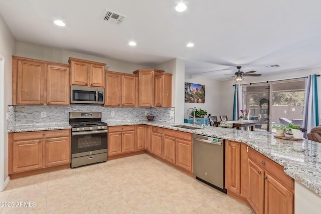 kitchen with visible vents, decorative backsplash, light stone counters, stainless steel appliances, and a sink