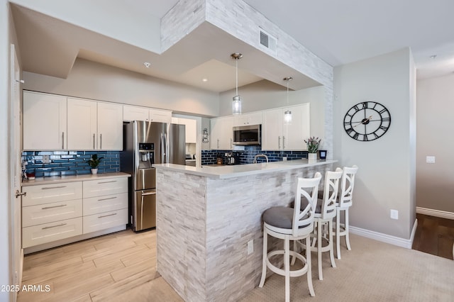 kitchen featuring a kitchen breakfast bar, a peninsula, appliances with stainless steel finishes, white cabinets, and light countertops