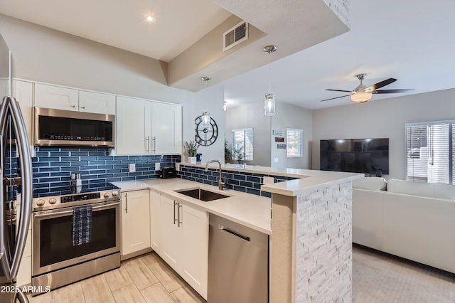 kitchen featuring tasteful backsplash, visible vents, a peninsula, stainless steel appliances, and a sink