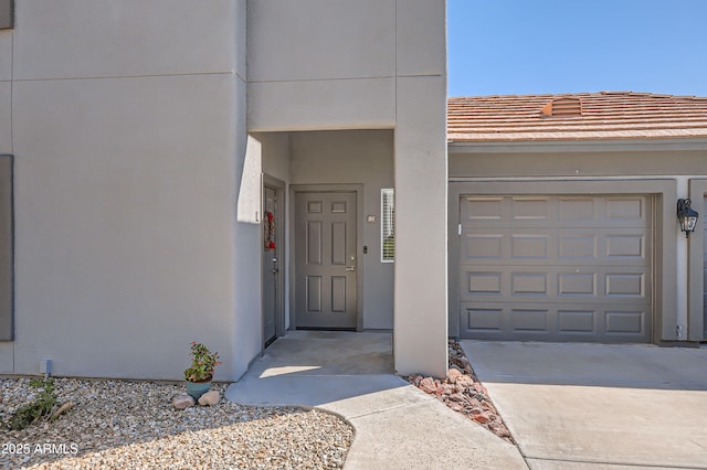 view of exterior entry with stucco siding, a tiled roof, concrete driveway, and a garage