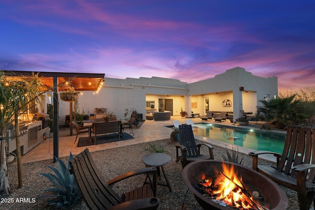 exterior space featuring an outdoor pool, an outdoor living space with a fire pit, a patio, and an outdoor kitchen