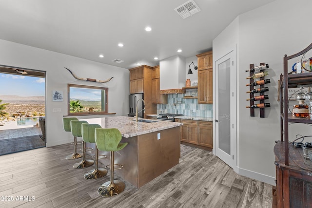 kitchen featuring stainless steel appliances, premium range hood, a sink, visible vents, and decorative backsplash