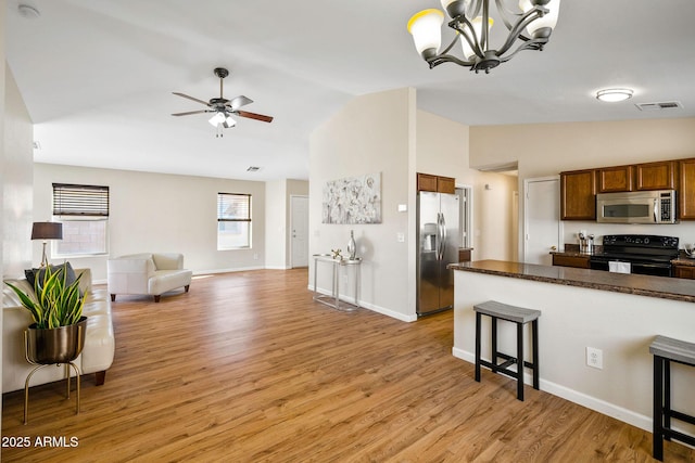 kitchen featuring dark countertops, open floor plan, stainless steel appliances, light wood-style floors, and pendant lighting