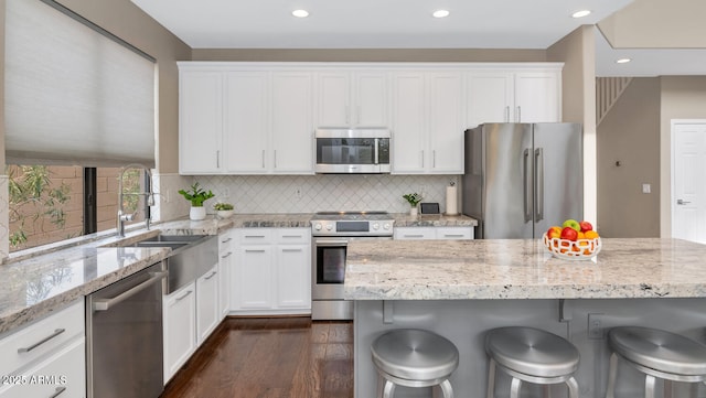 kitchen with white cabinets, dark wood-style floors, stainless steel appliances, a kitchen bar, and a sink