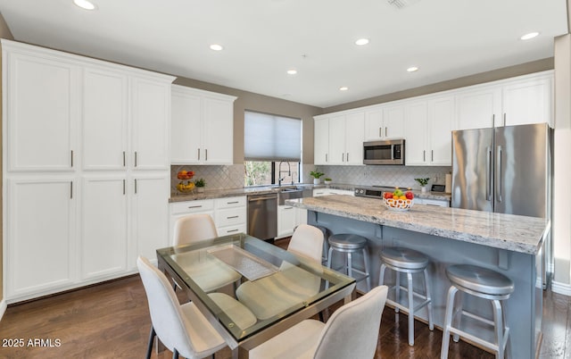 kitchen with dark wood-style flooring, stainless steel appliances, white cabinetry, a kitchen island, and a kitchen breakfast bar