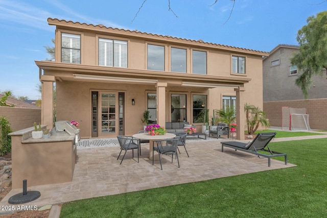 rear view of house featuring a patio, a lawn, fence, and stucco siding