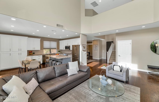 living area featuring dark wood-type flooring, visible vents, baseboards, and stairs