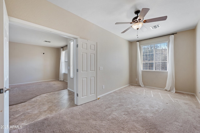 carpeted empty room featuring tile patterned floors, baseboards, visible vents, and ceiling fan