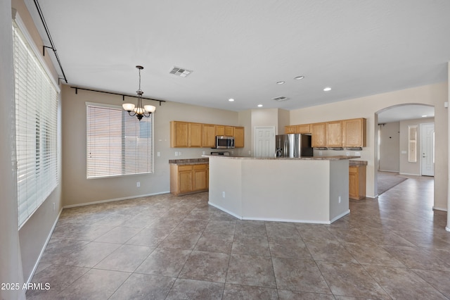 kitchen featuring visible vents, an island with sink, appliances with stainless steel finishes, an inviting chandelier, and arched walkways