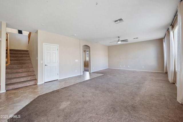 unfurnished living room featuring stairway, carpet, visible vents, arched walkways, and ceiling fan