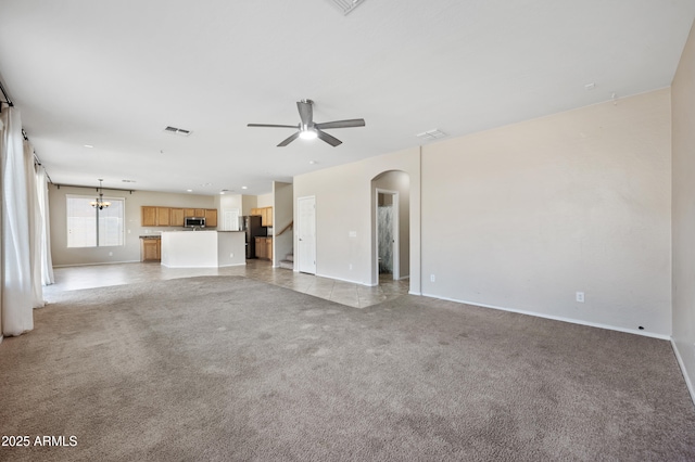 unfurnished living room featuring light carpet, visible vents, arched walkways, and ceiling fan