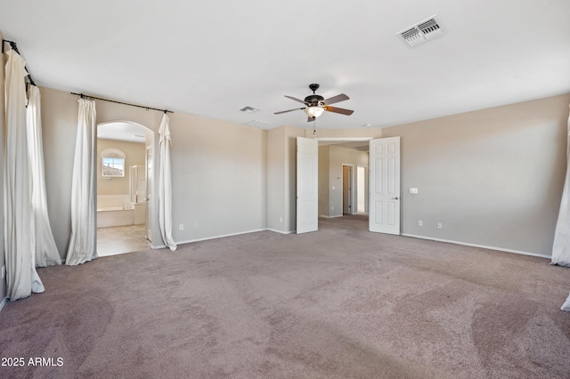 carpeted spare room featuring visible vents, arched walkways, baseboards, and a ceiling fan