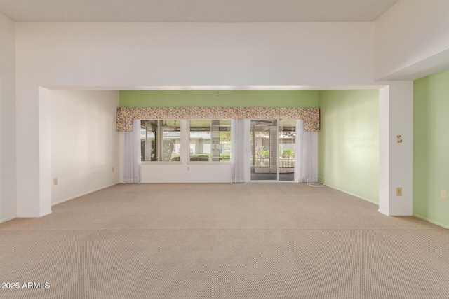 carpeted spare room featuring a towering ceiling and baseboards