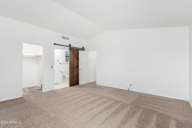 unfurnished bedroom with vaulted ceiling, a spacious closet, light carpet, and a barn door