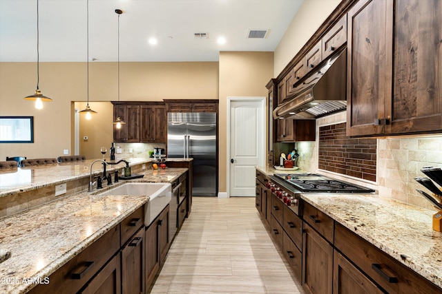 35971 N Prickley Pear Rd, Cave Creek, AZ 85331 - kitchen featuring stainless steel appliances, under cabinet range hood, dark brown cabinetry, light stone counters, and backsplash