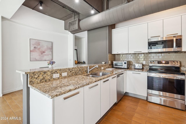 kitchen with kitchen peninsula, appliances with stainless steel finishes, white cabinets, and sink