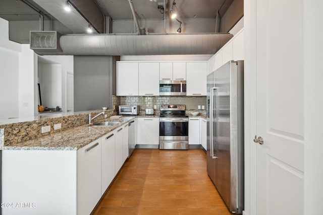 kitchen with light stone countertops, sink, stainless steel appliances, kitchen peninsula, and white cabinets