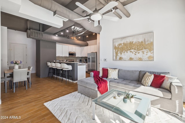 living room with a towering ceiling, light hardwood / wood-style flooring, and ceiling fan