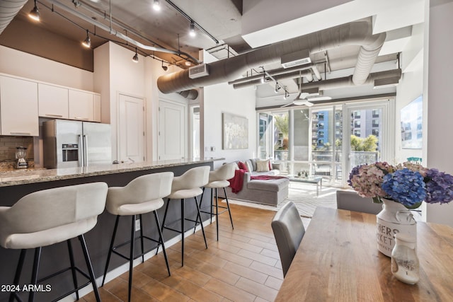 kitchen with backsplash, stainless steel refrigerator with ice dispenser, a towering ceiling, light stone counters, and white cabinetry